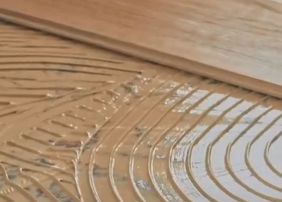 Padrão curvo em relevo numa superfície castanha húmida sobre madeira clara.