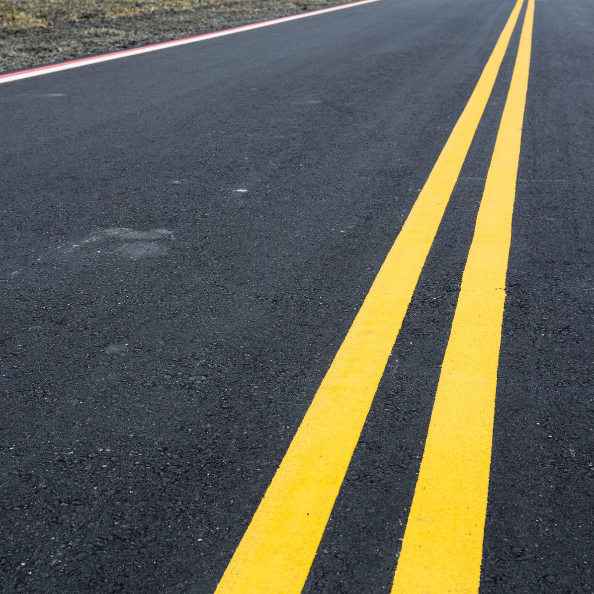 Troço de estrada asfaltada com linhas amarelas contínuas ao centro
