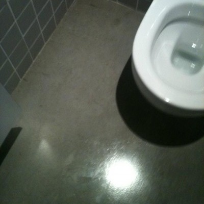 Vaso sanitário branco num chão cinza polido e paredes de azulejos cinzentos