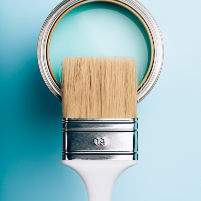 Pincel de pintura com cerdas naturais à frente de lata aberta de tinta azul clara