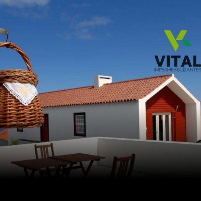 Cesta de vime pendurada com pano branco, casa branca com portas vermelhas e telhado vermelho ao fundo e logo 'VITAL IMPERMEABILIZANTES'