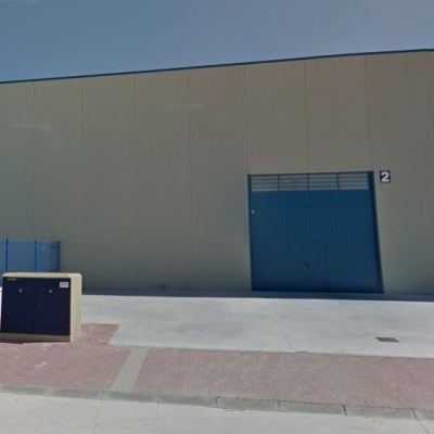 fachada industrial cinzenta com porta azul e passeio em dia de céu limpo