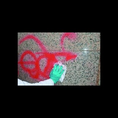 Pessoa com luva verde a limpar grafite vermelho numa parede de mármore bege