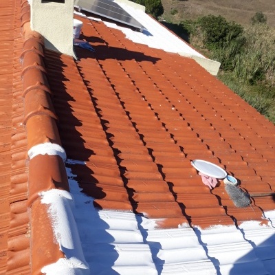 Telhado com telhas cerâmicas vermelhas parcialmente pintadas de branco com pincel e tinta