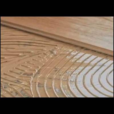 Padrão curvo em relevo numa superfície castanha húmida sobre madeira clara.