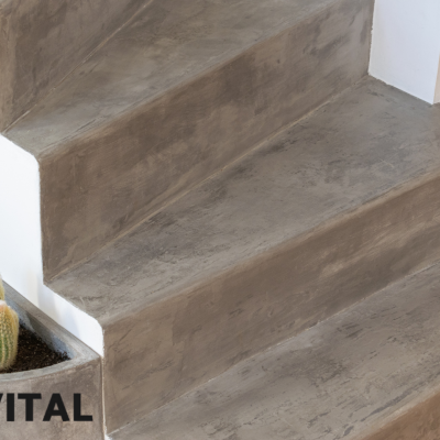 Escada interior em betão cinzento com textura lisa, parede branca, vaso com cactos ao lado.