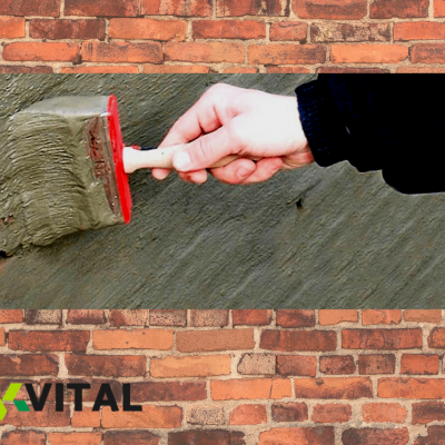 Mão a aplicar argamassa cinzenta numa parede com espátula vermelha e branca, logótipo VITAL no canto
