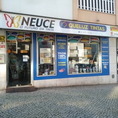 Fachada de loja de tintas com letreiros e vitrines mostrando baldes de tinta