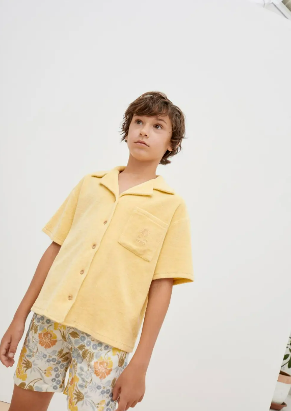 Menino com camisa amarela e calções florais sobre fundo branco