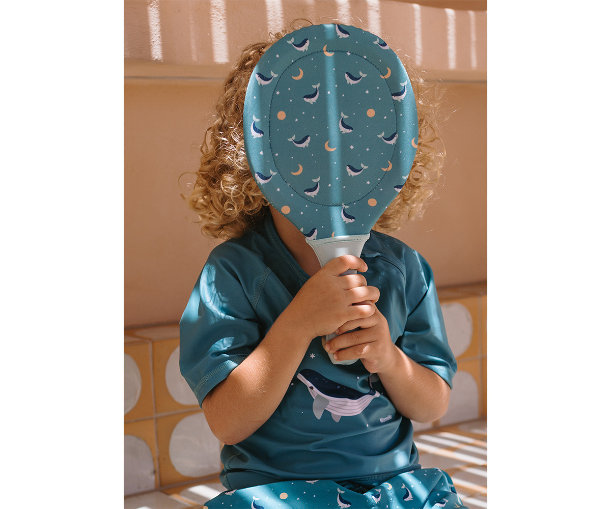 Criança com roupa azul-petróleo e raquete com padrão de golfinhos