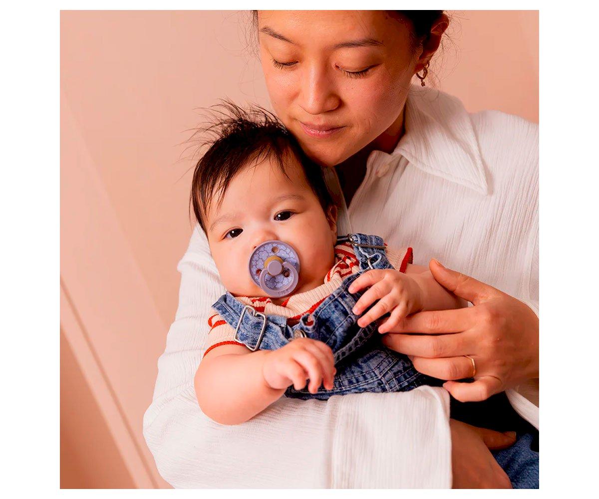 Mulher a segurar bebé com chupeta azul e roupa laranja e azul