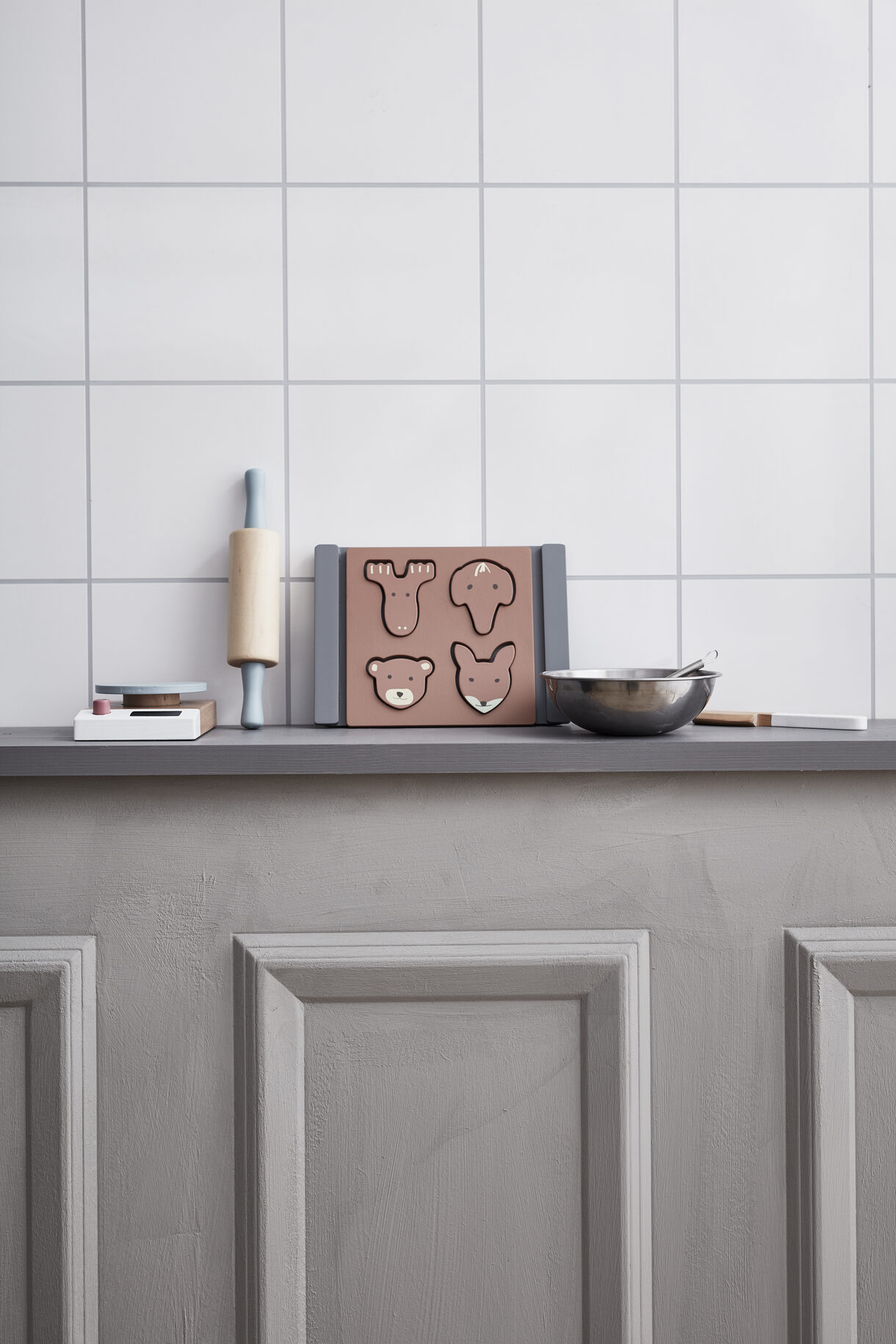 Bancada com utensílios de cozinha e formas animais em madeira sobre fundo de azulejos brancos