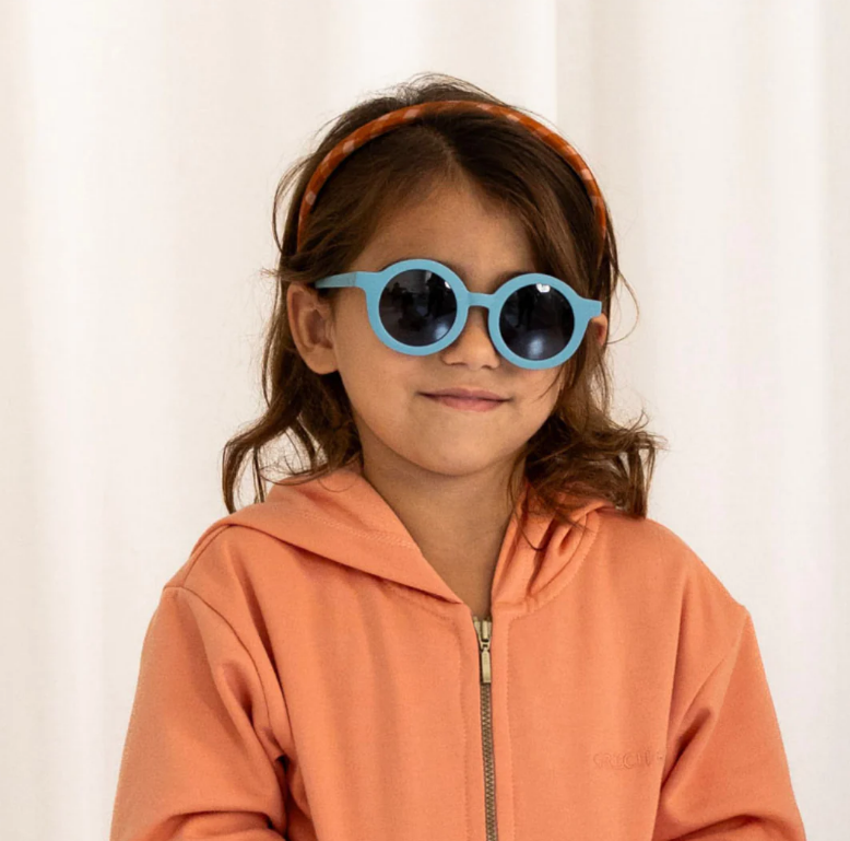 Criança com óculos de sol azuis e casaco laranja