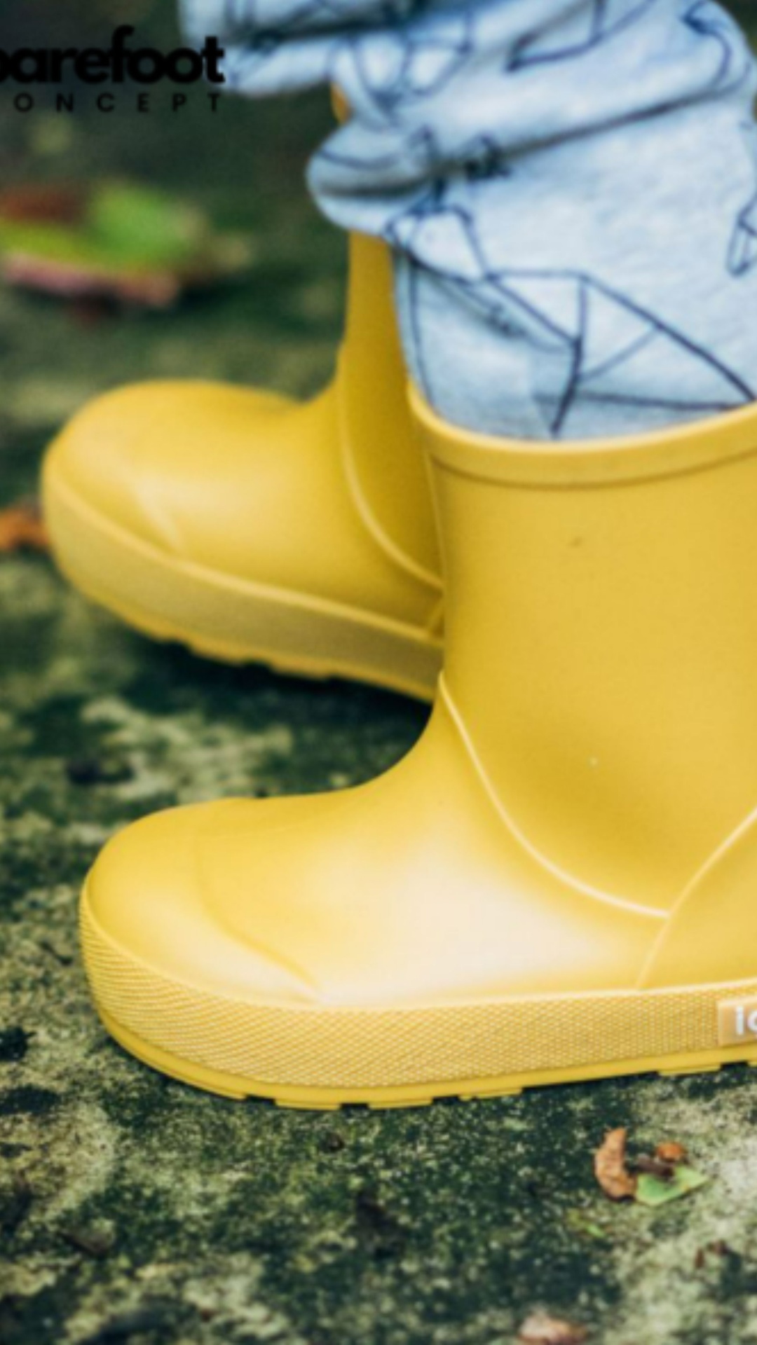 Botas impermeáveis amarelas para criança com calças cinzentas num chão exterior