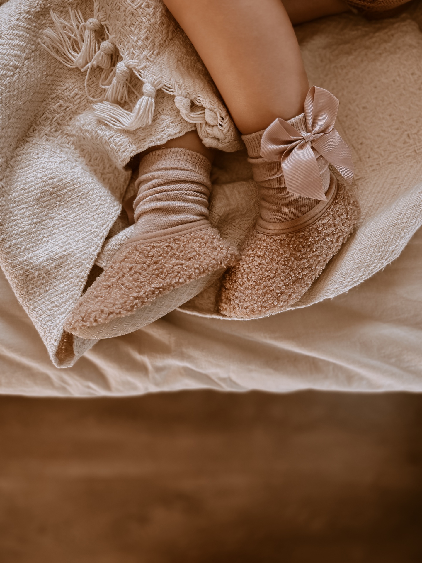 Meias castanhas com laço e sapatinhos felpudos castanhos em criança sobre cobertor bege.