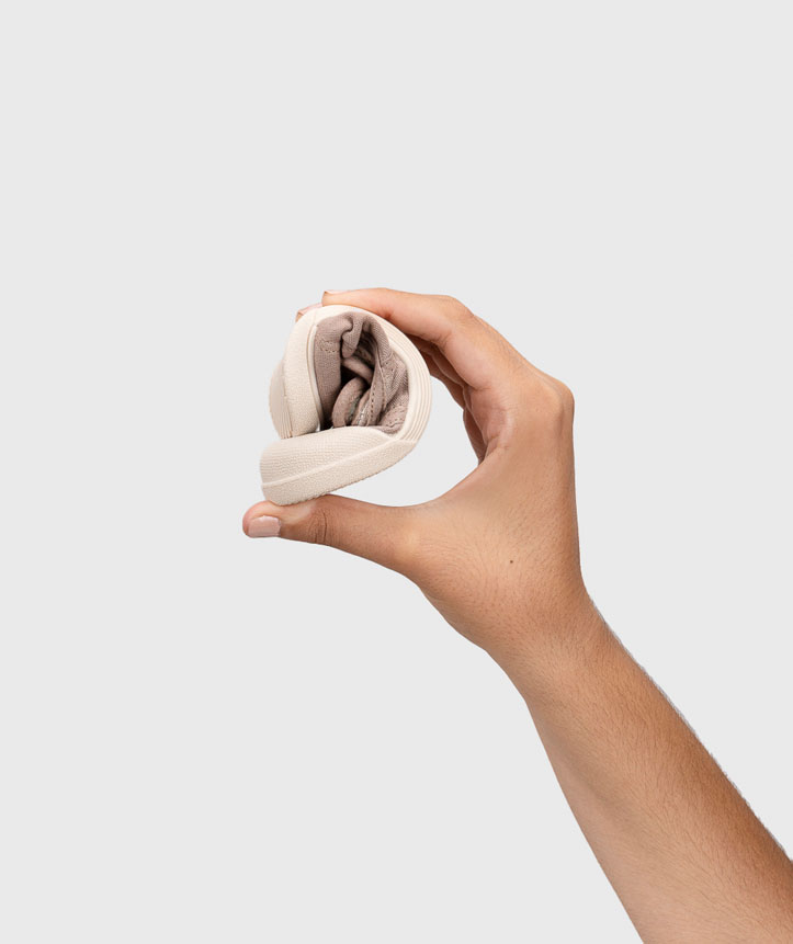 Mão a segurar sapatilha dobrada bege claro em fundo branco