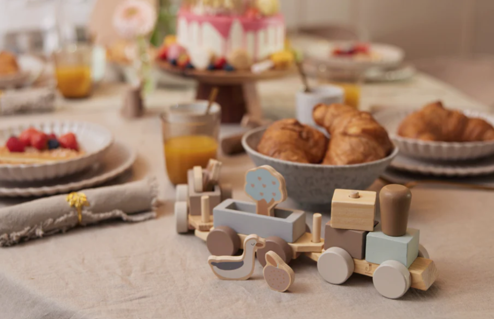 Mesa de pequeno-almoço com croissants, sumo, sobremesas, bolo decorado e comboio de brinquedo de madeira