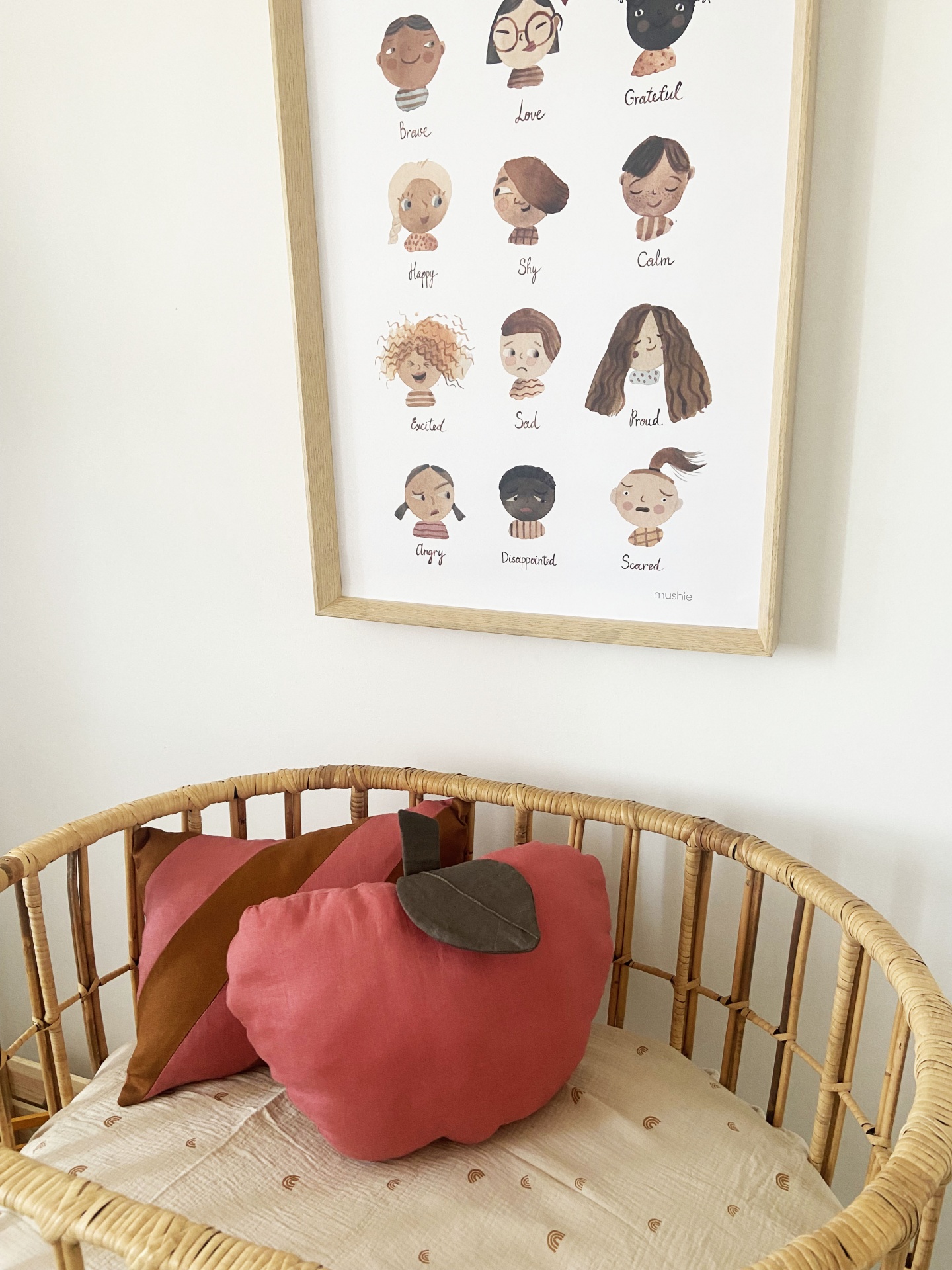 Almofadas em forma de folha e maçã vermelha no berço de vime com quadro de ilustrações na parede