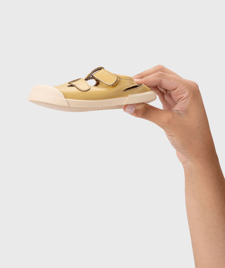 Sapato infantil bege com tiras de velcro e sola branca segurado por uma mão