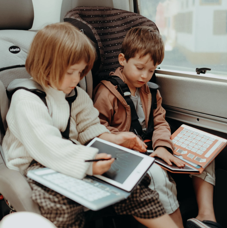 Duas crianças em assentos de carro com tablets e cintos de segurança