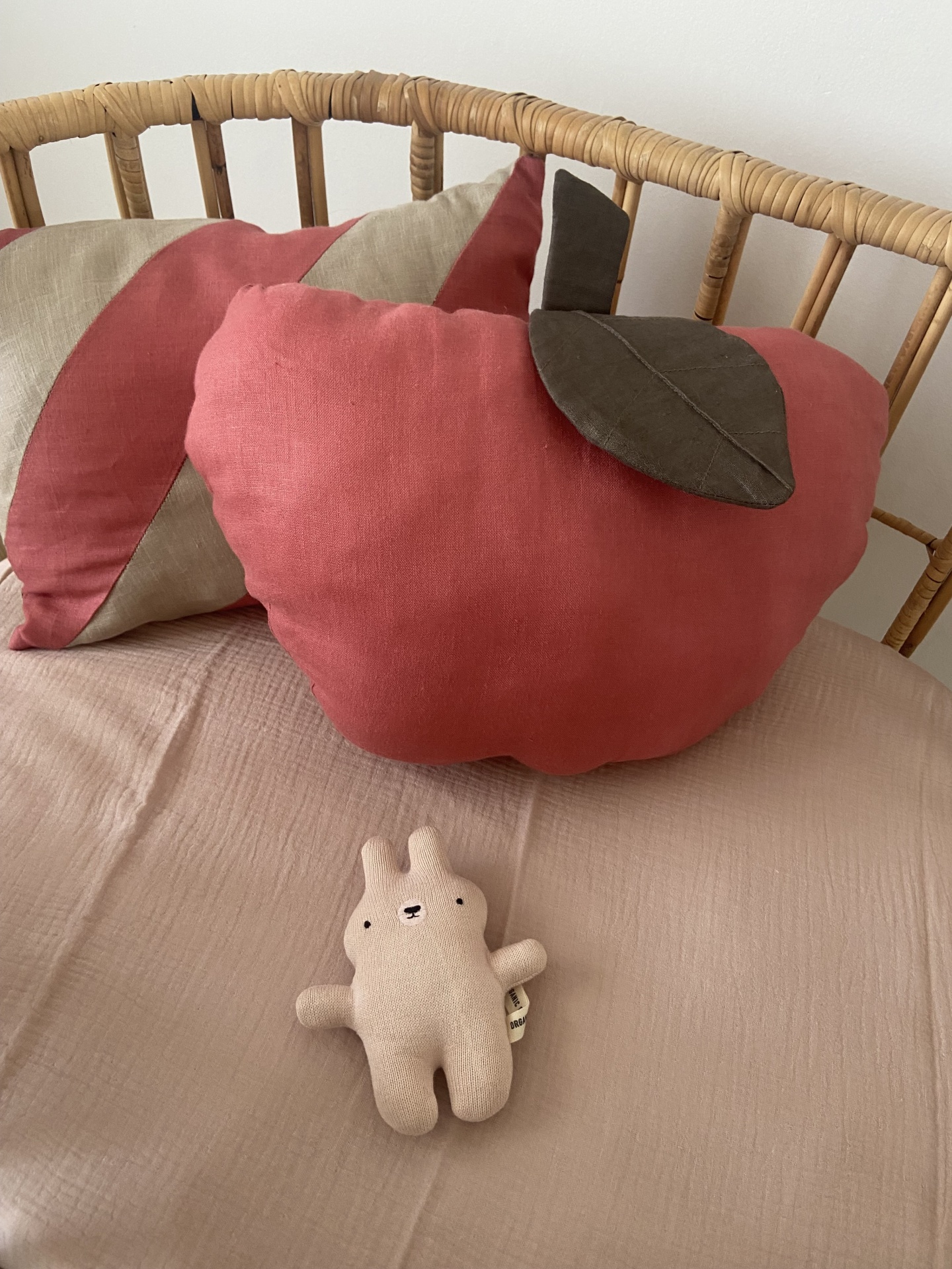 Almofadas coloridas e brinquedo de peluche numa cama com cabeceira de vime