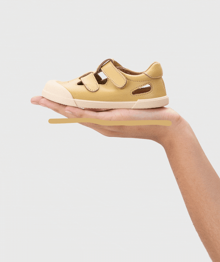 Tênis infantil bege com velcro e sola branca na mão.