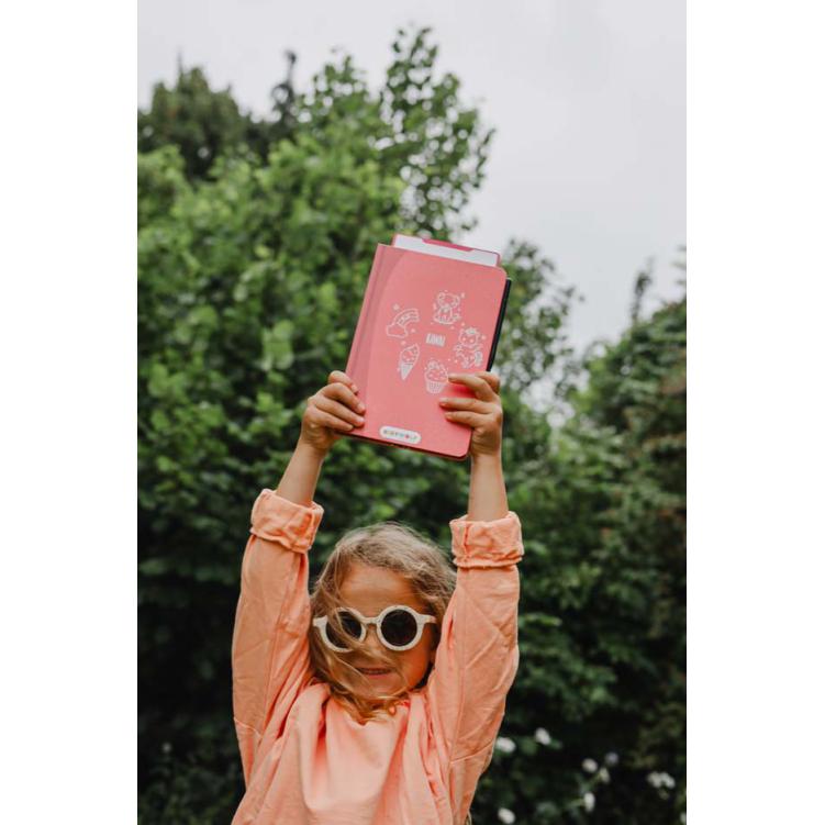 Caderno rosa com ilustrações, criança com óculos e camisa cor de pêssego ao ar livre