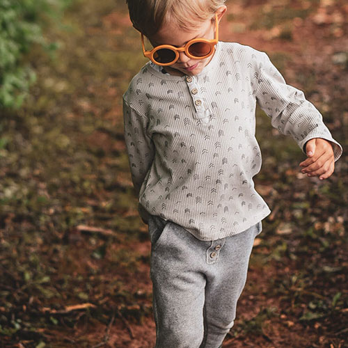 Criança com óculos de sol e roupa bege e cinza numa caminhada ao ar livre