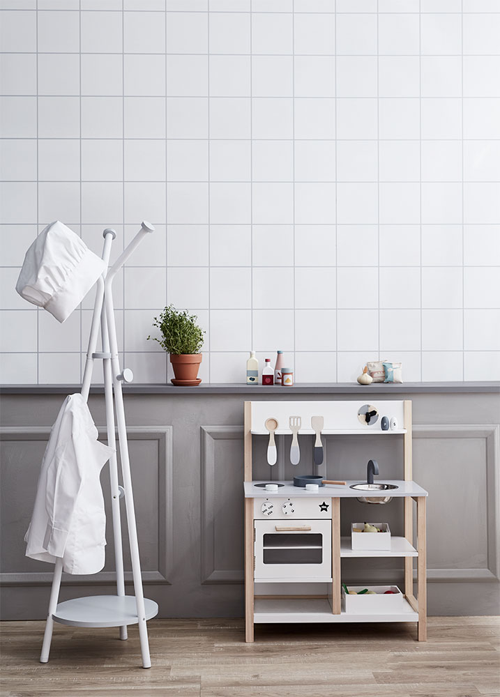 Cozinha de brincar em madeira clara e branca com utensílios e cabide branco com roupa pendurada