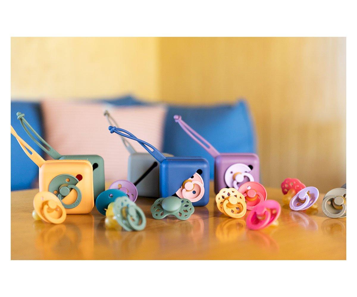 Caixas de transporte coloridas com chupetas variadas em cima de uma mesa de madeira