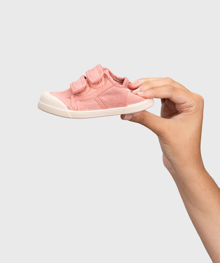 Sapatilha infantil rosa com velcro segurada por mão em fundo cinza