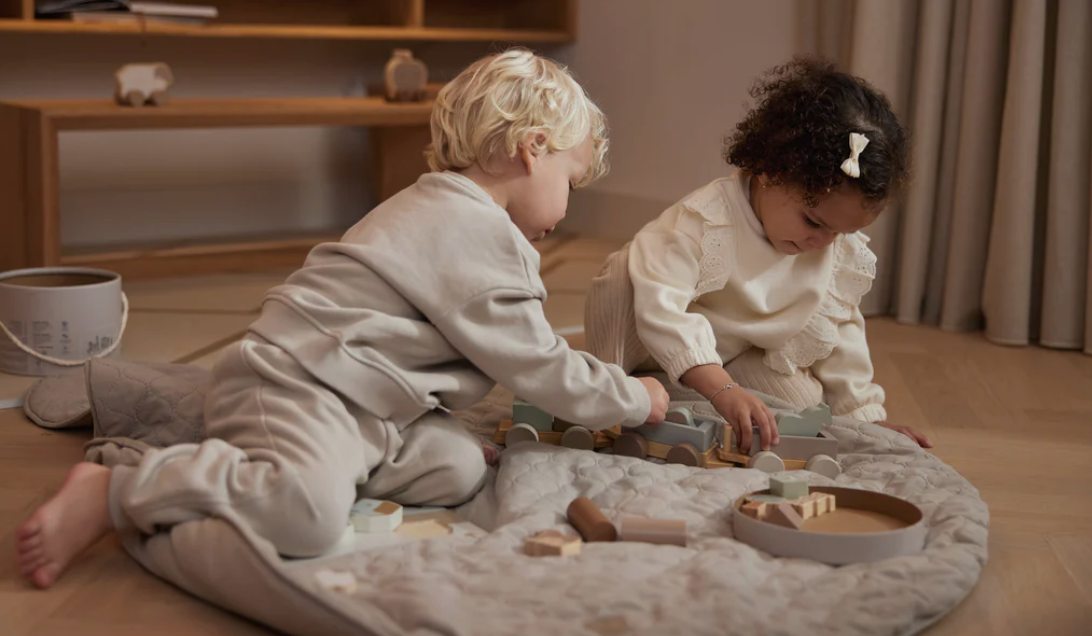 Crianças brincando com blocos de madeira em tapete cinza acolchoado