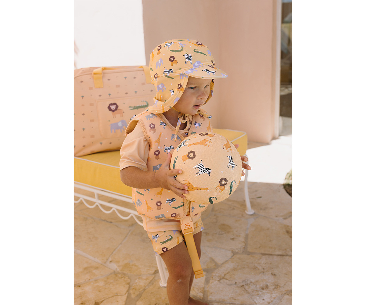 Criança com colete salva-vidas e chapéu estampados segurando bola estampada, ao ar livre