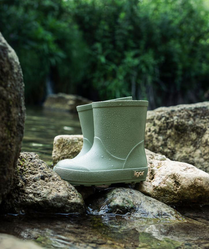 Botas verdes de borracha com gotas de água sobre pedras junto ao riacho