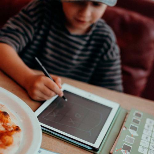 Criança a usar tablet com caneta digitalizadora ao lado de pizza e teclado