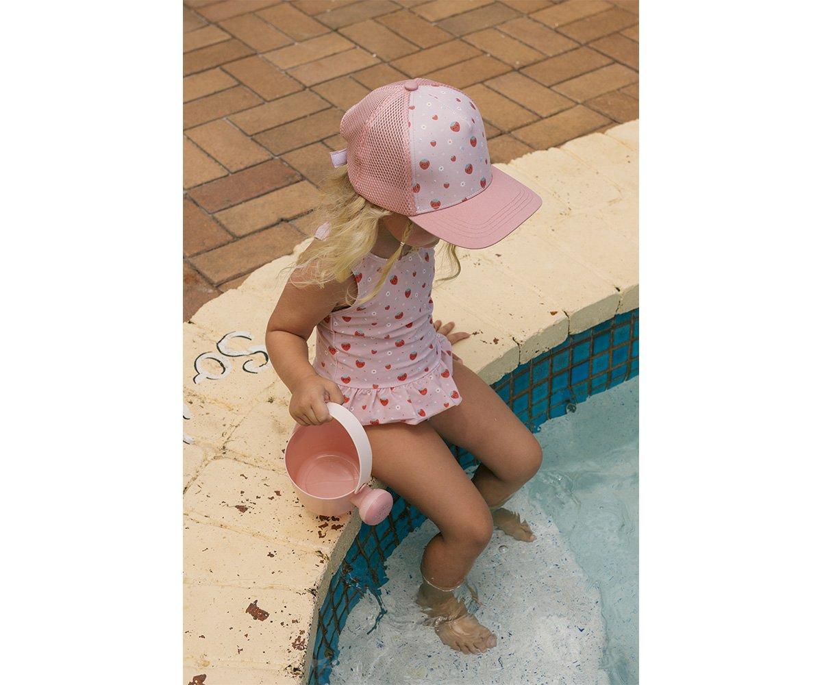Criança com fato de banho e boné rosas sentada na borda da piscina