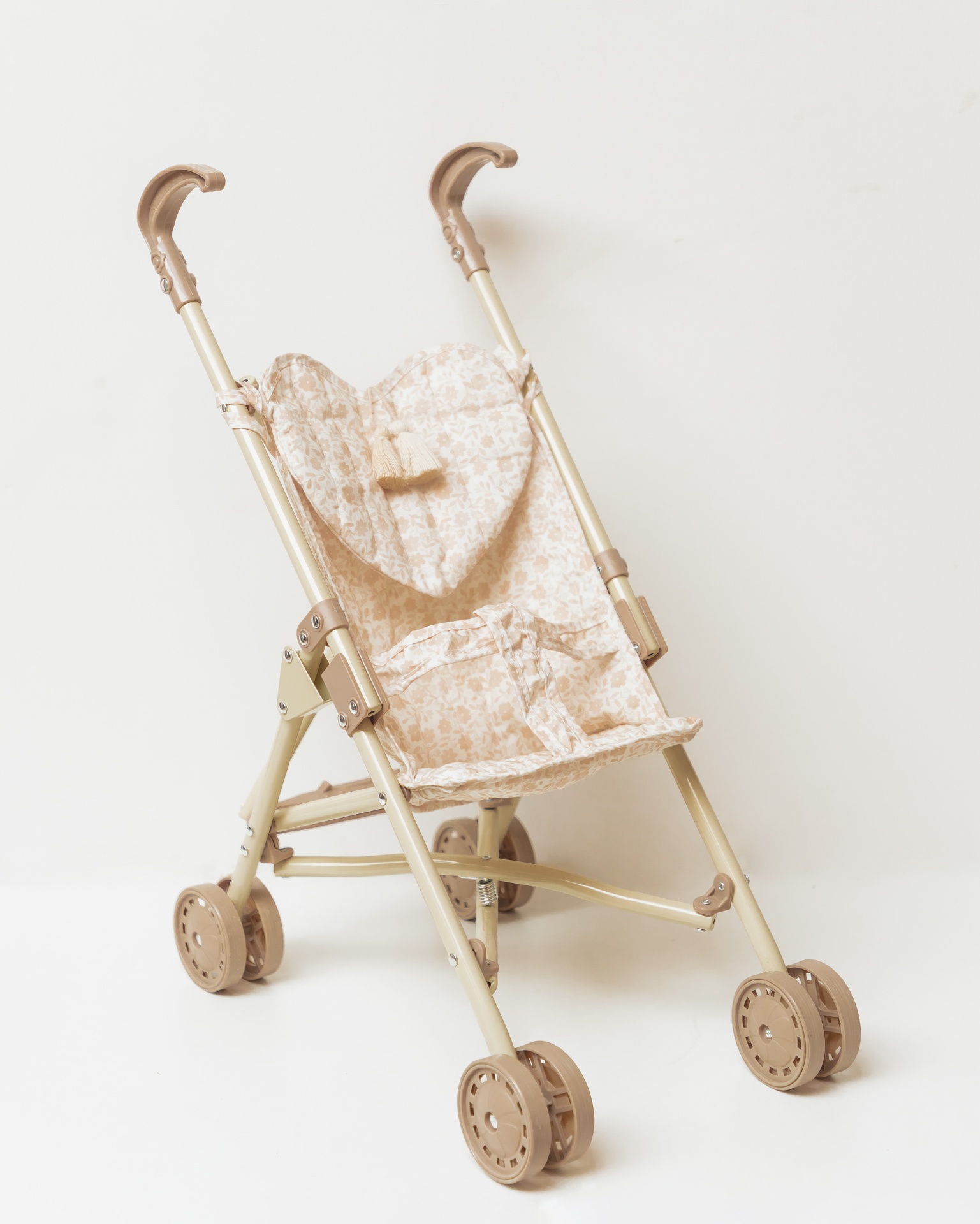 Carrinho de boneca bege com padrão floral, rodas e alças curvas.