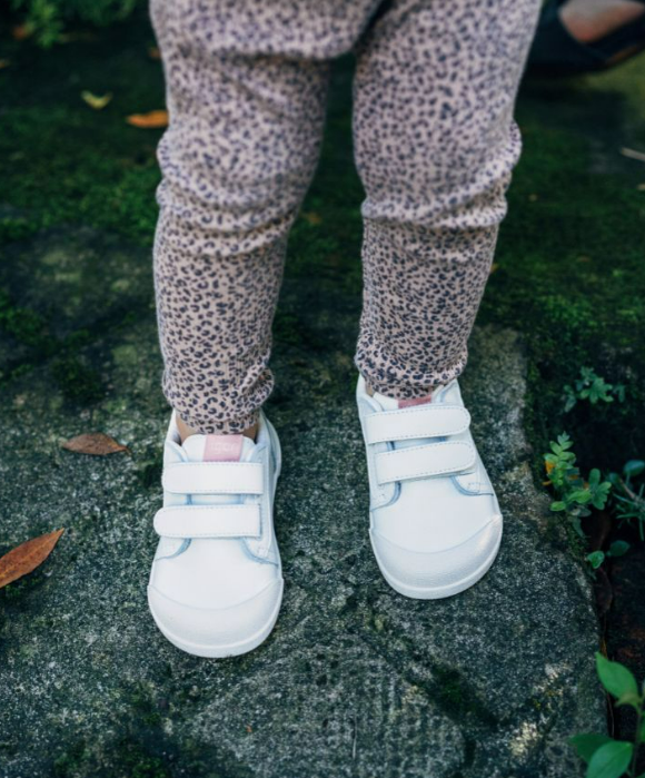 Sapatos brancos infantis de velcro usados com calças florais sobre pedra