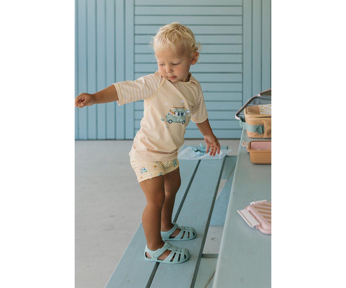 Criança loira em túnica e sandálias azuis em banco de madeira azul