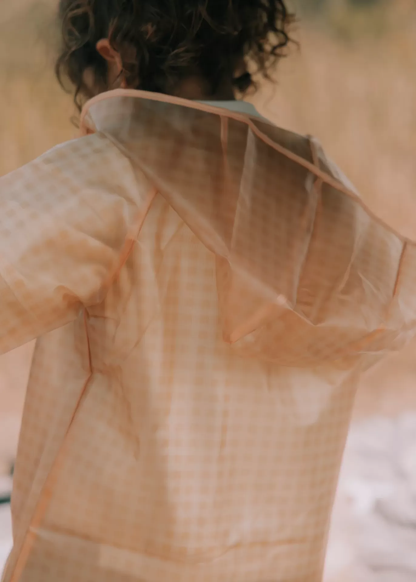 Capa de chuva transparente com acabamento laranja claro vista de costas