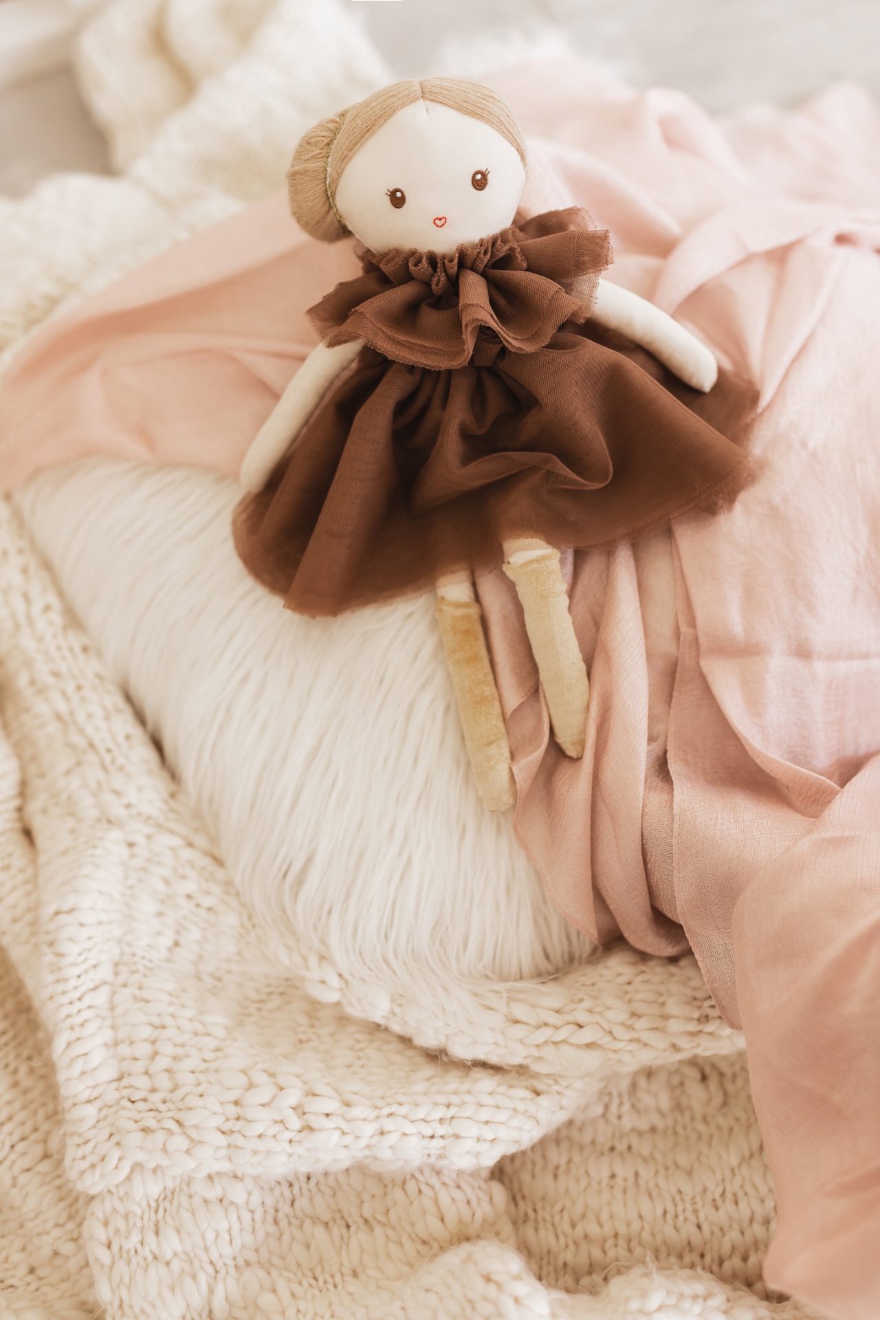 Boneca de pano com vestido castanho sobre almofadas e mantas acolhedoras