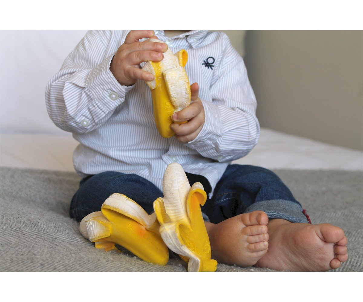 Criança sentada segurando brinquedos de banana descascada amarelos e brancos