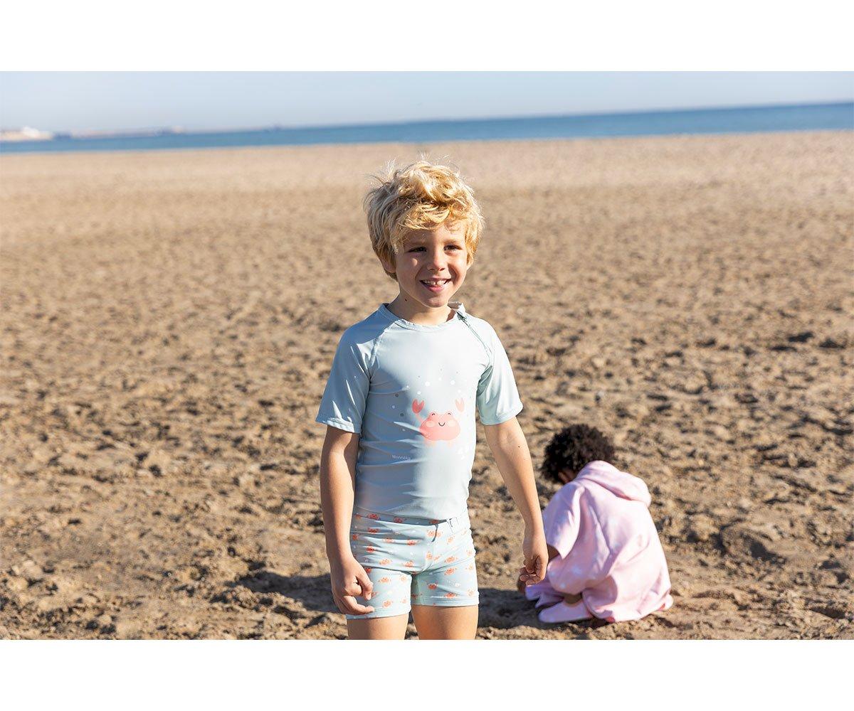 Criança com roupa de banho azul claro com estampa de caranguejo na praia