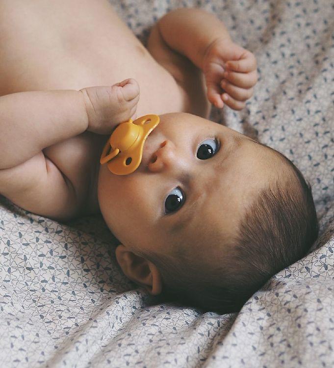 Bebé deitado com chupeta amarela em tecido estampado