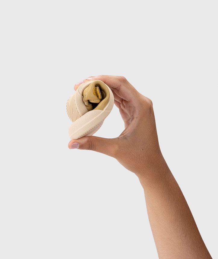 Sapato flexível bege segurado por uma mão sobre fundo branco