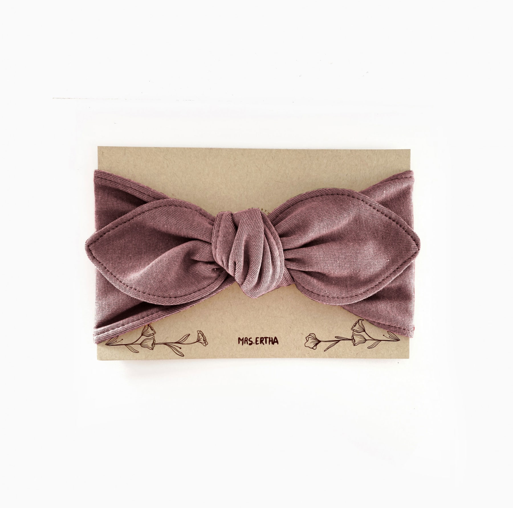 Faixa de cabelo em veludo lavanda com nó central em cartão bege com desenhos florais e marca.