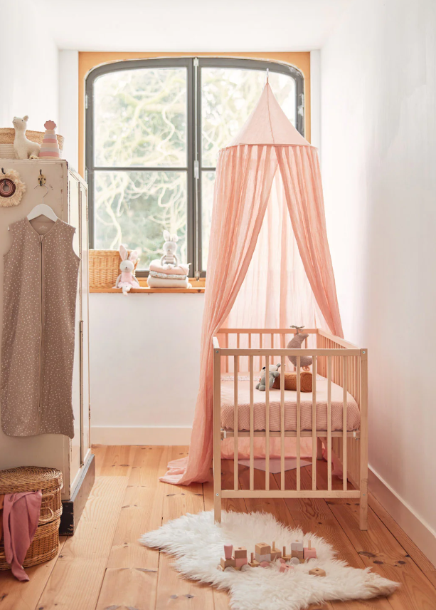 Berço de bebé com rede rosa translúcida em quarto claro de madeira