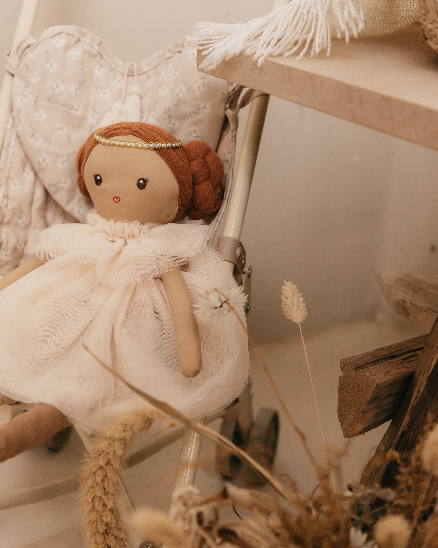 Boneca de tecido com vestido branco sentada numa cadeira com almofada bege floral