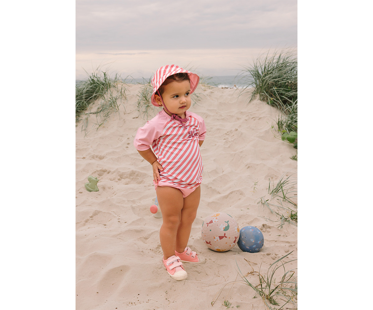 Criança na praia com fato de banho rosa e chapéu listrado