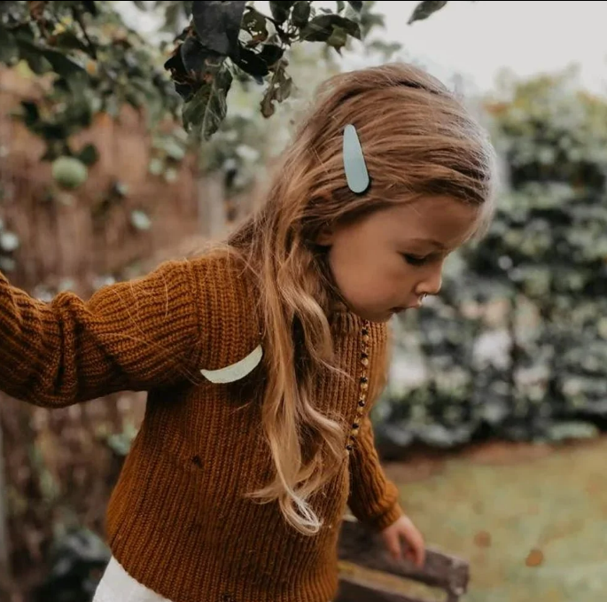 Menina com casaco castanho e ganchos de cabelo azul em ambiente exterior